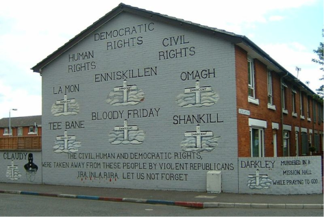 Loyalist mural in east Belfast. This mural displays the words “The civil human and democratic rights taken away from these people by violent republicans IRA, INLA, RIRA. Let us not forget.” It lists names of places (towns and buildings) that were attacked and prominent events, like Bloody Friday that added fire to flame during The Troubles. The mural displays a cross for all of the cited sources of turmoil.